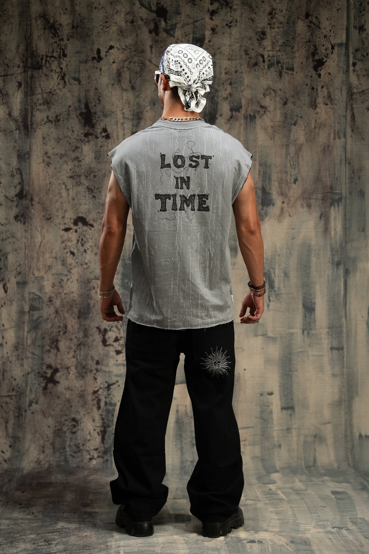 Person wearing a sleeveless shirt with 'Lost in Time' text, standing against a textured wall.