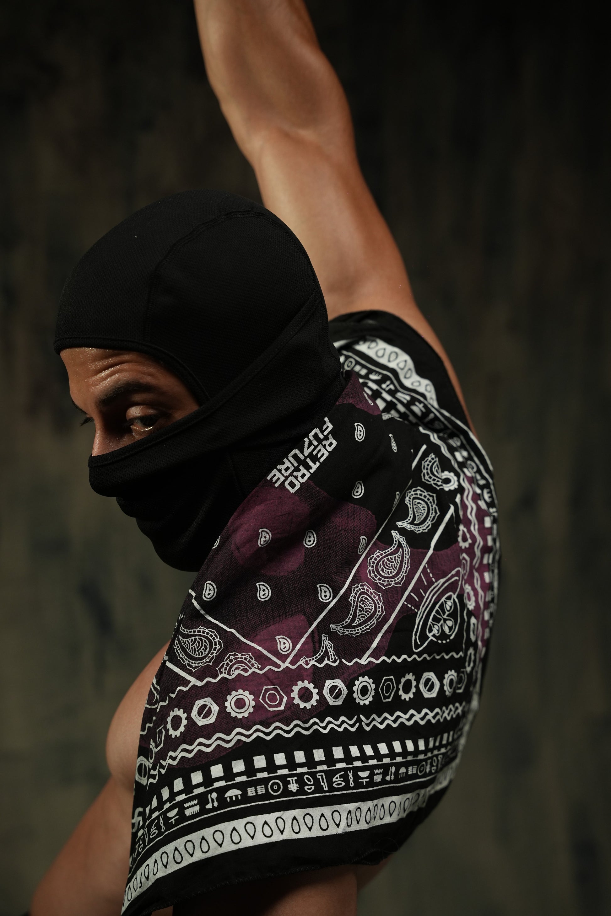Person wearing a black balaclava and patterned shorts against a dark background
